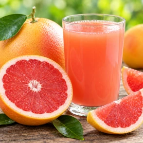 Jugo de pomelo o toronja natural junto a pomelos frescos